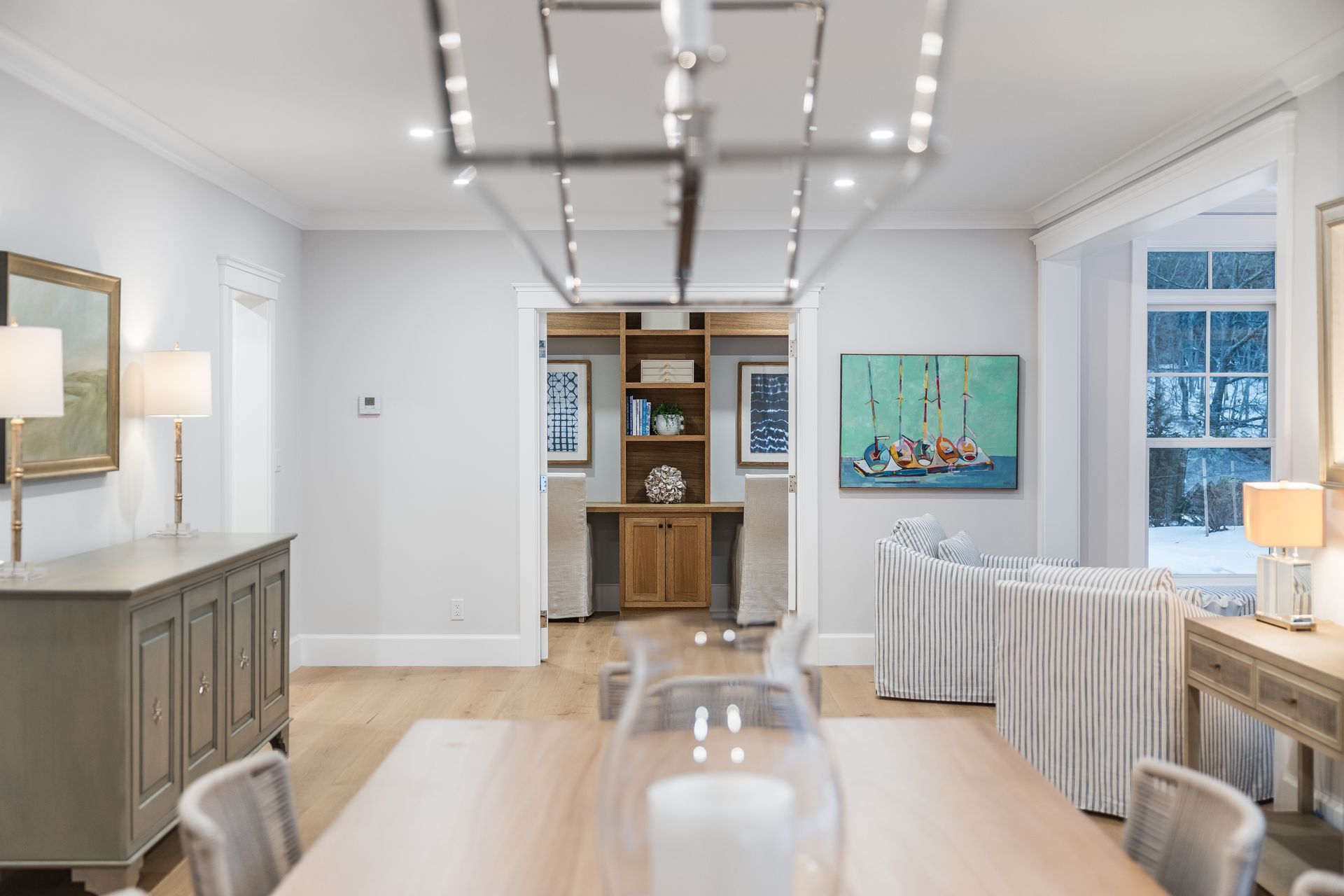 Dining room with light-colored walls, wood floors, and neutral furniture. A rectangular light fixture hangs above a dining table.