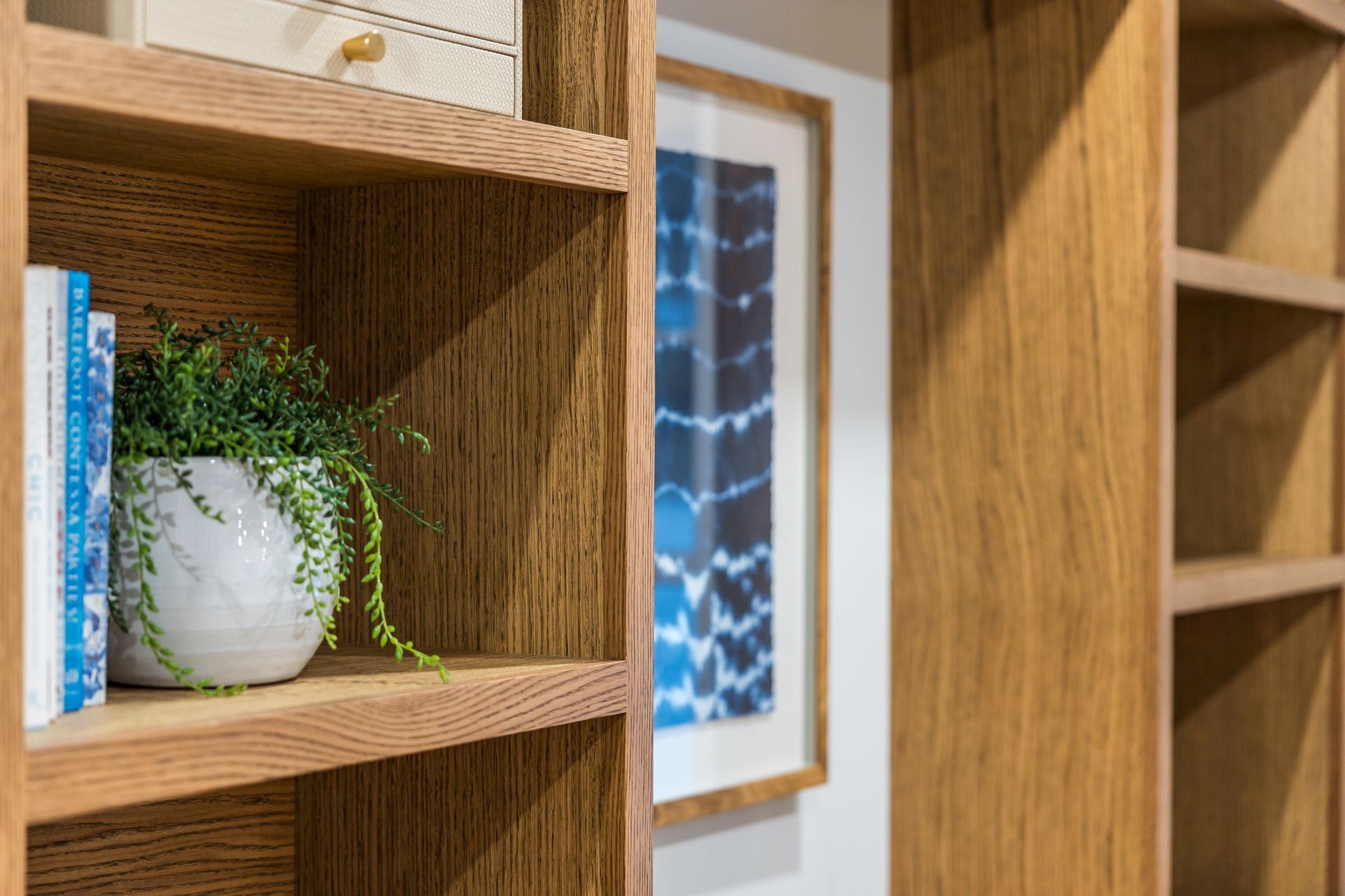 Wooden bookshelves with books, a plant, and framed artwork.