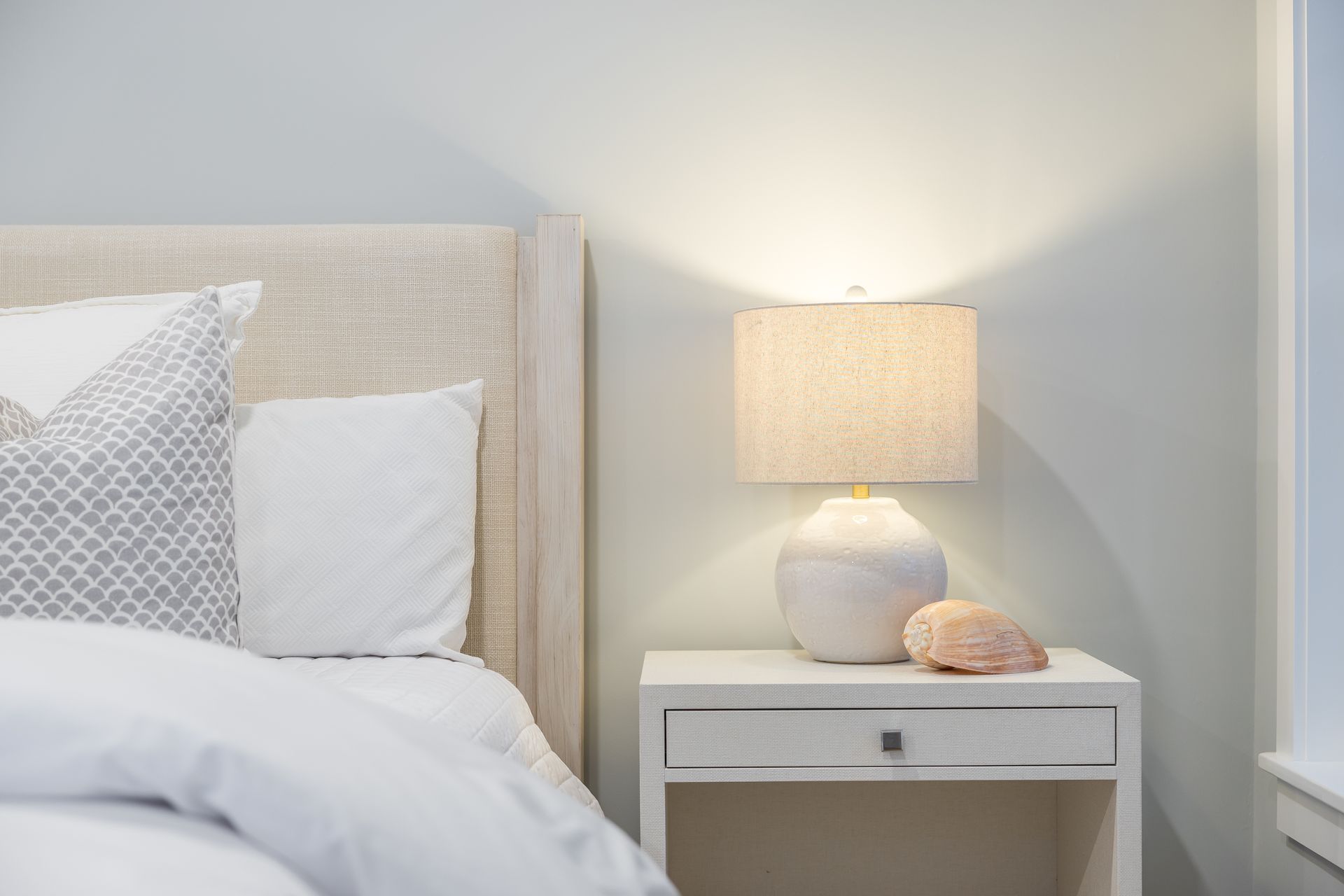Bedroom with bed, nightstand, lamp, and pillows in a neutral color palette.
