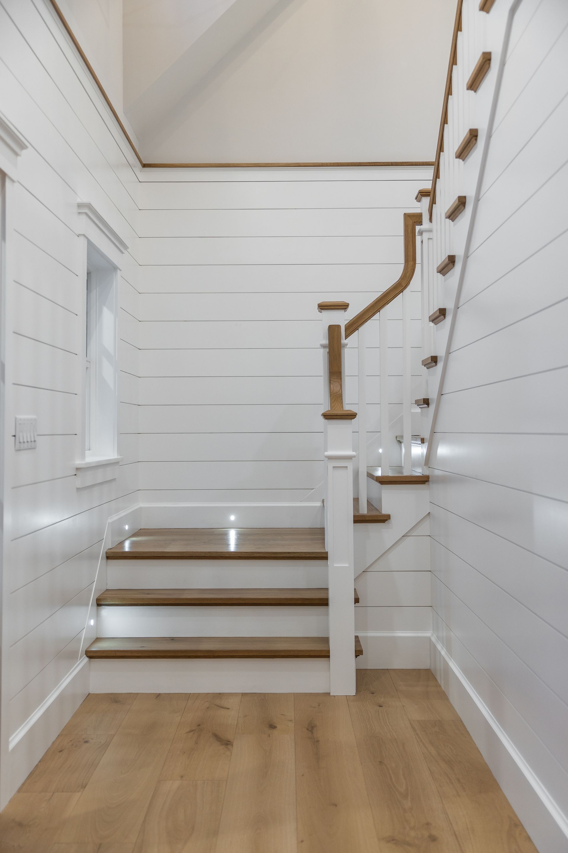 White paneled staircase with wooden steps and railing, light wood floors and walls.