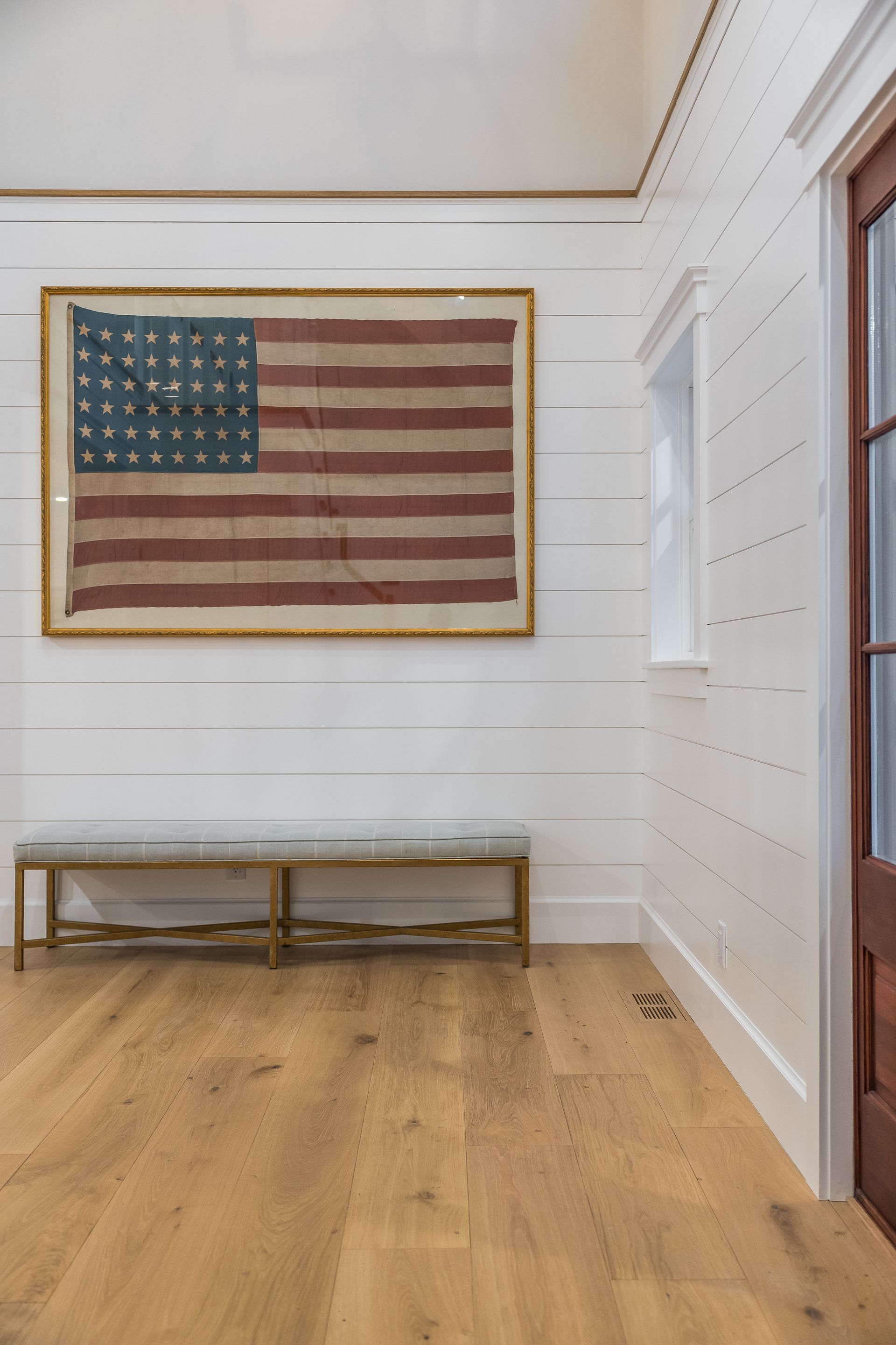 USA flag in a gold frame above a bench; hardwood floors, white paneled walls, and a door are visible.
