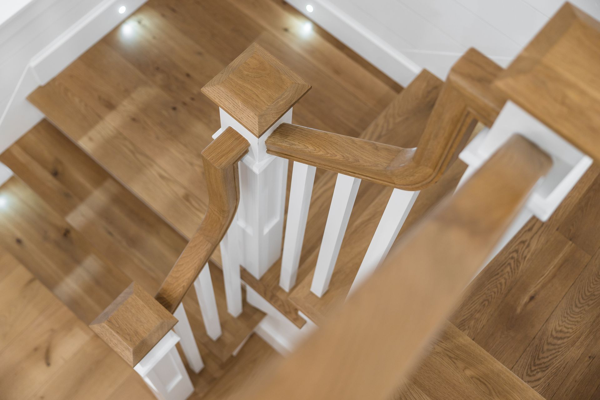 Overhead view of wooden staircase with white balusters and wooden handrail.