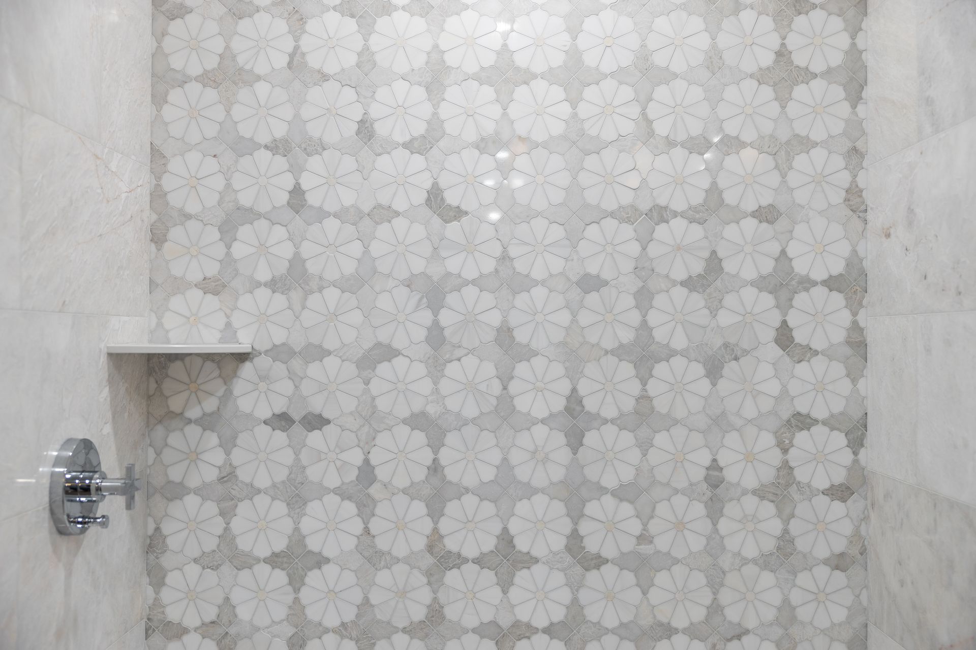 Shower interior with floral mosaic tile accent wall, built-in shelf, and chrome fixtures.