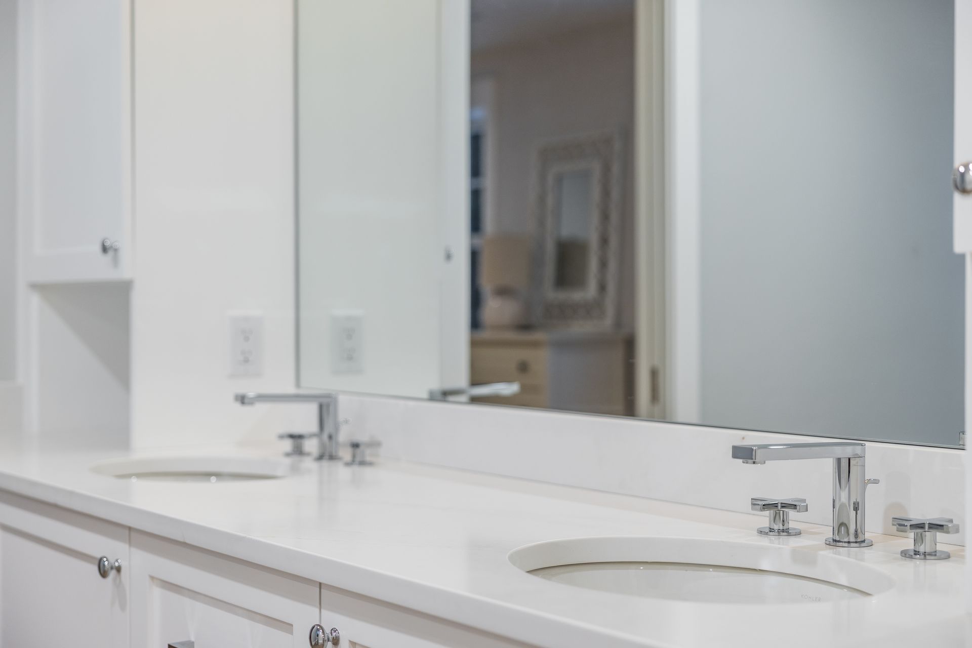 White bathroom with a long countertop, two sinks, and a large mirror reflecting the room.