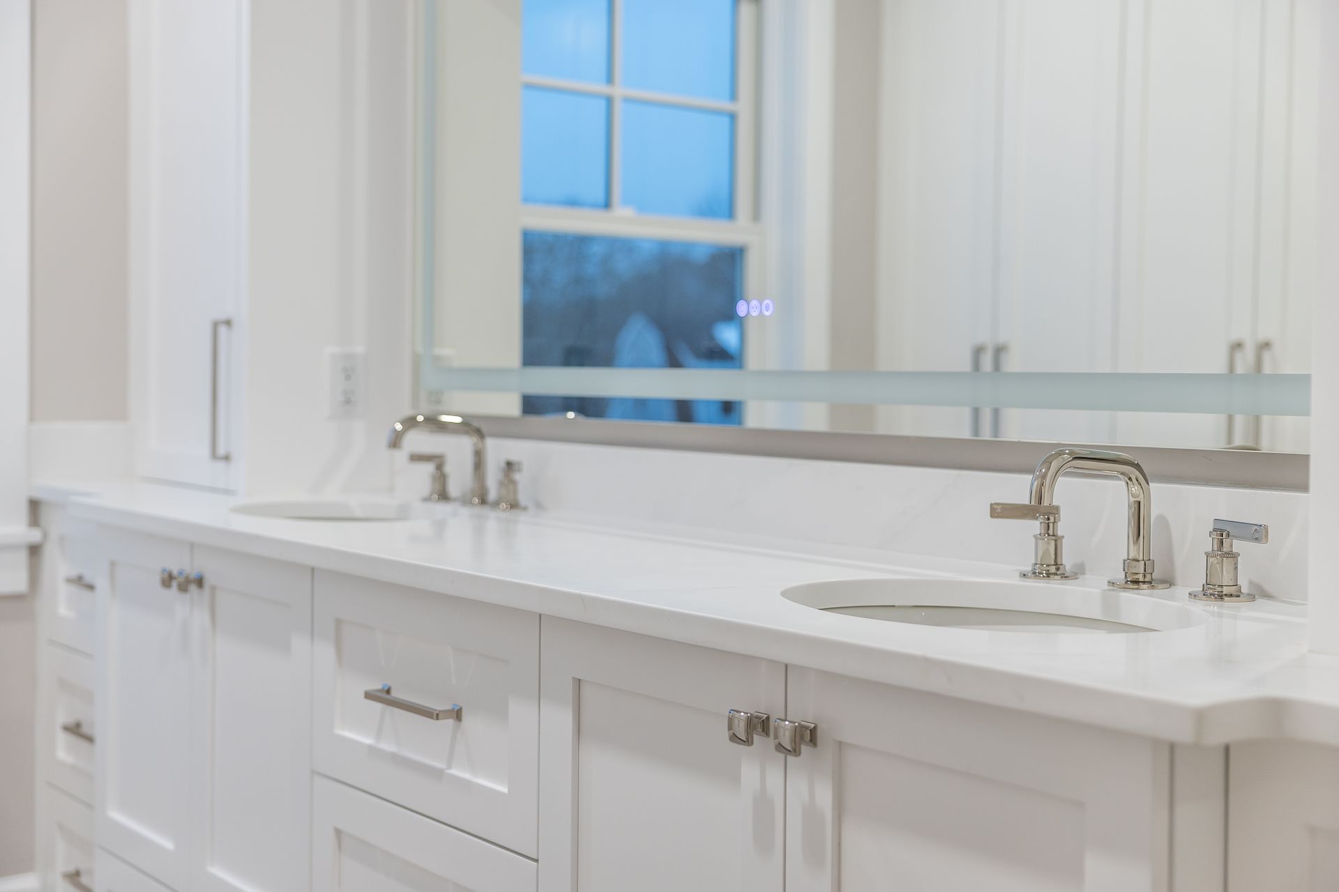 White bathroom vanity with two sinks, chrome faucets, and a large mirror.