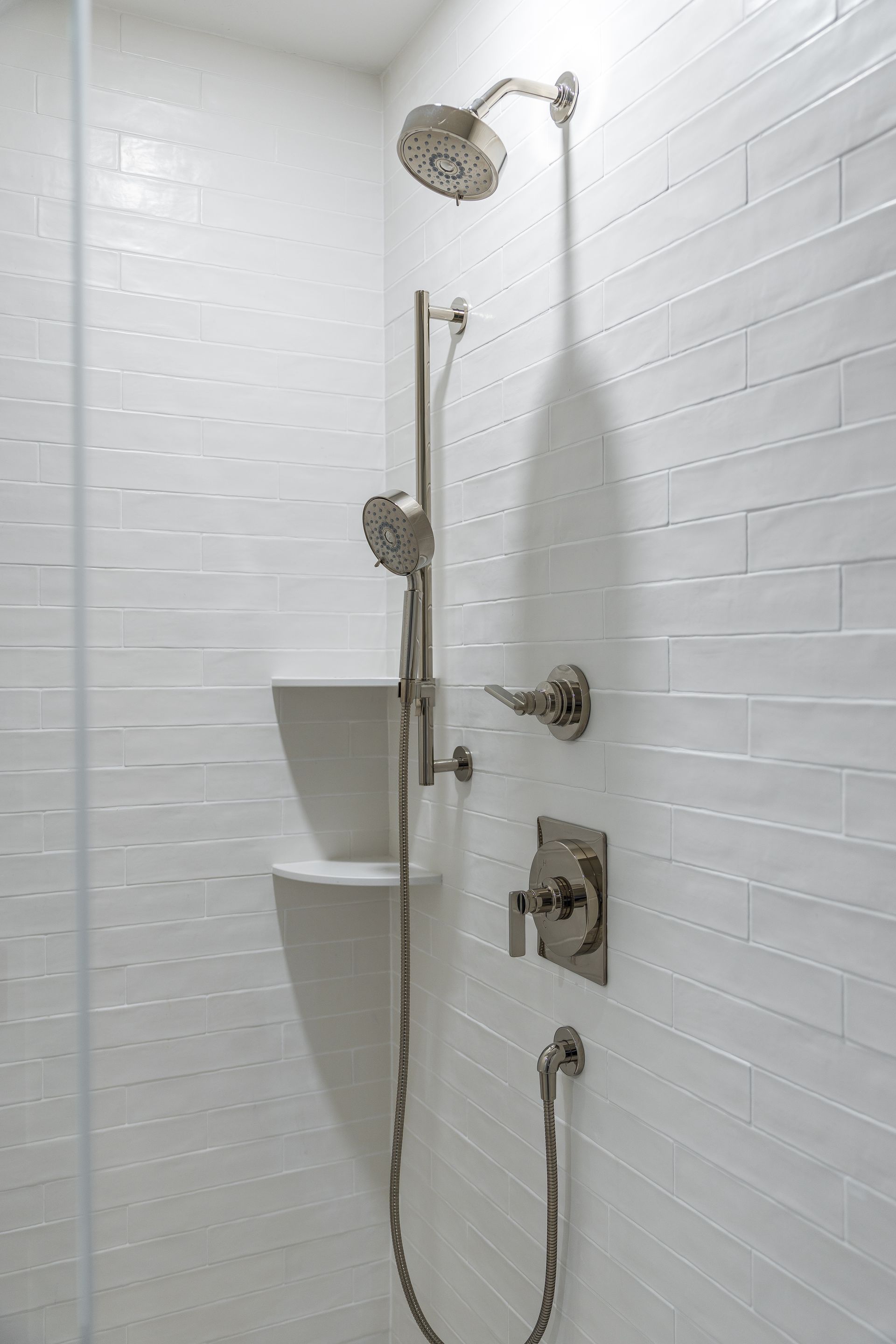Shower with silver fixtures against white tiled walls.