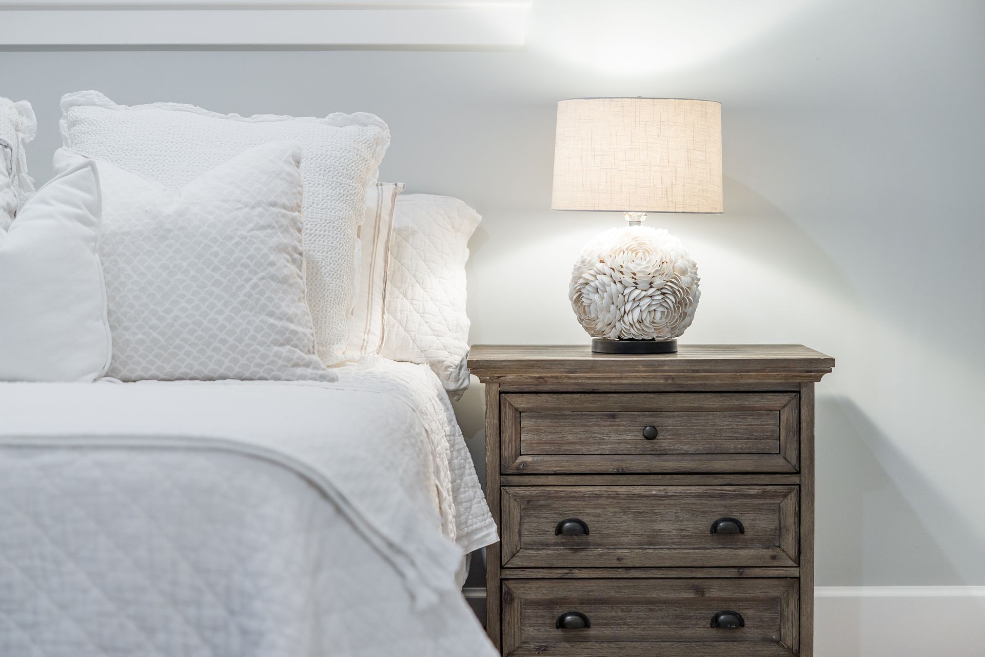 Bedroom with white bedding, nightstand, and lit lamp.
