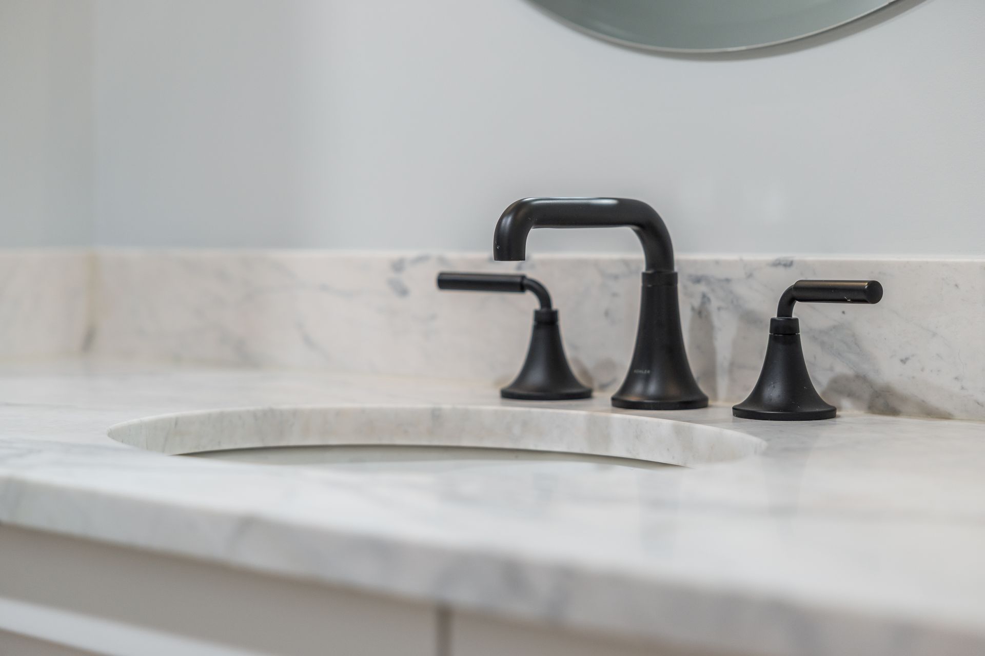 Black faucet and handles on a white marble countertop with an integrated sink.