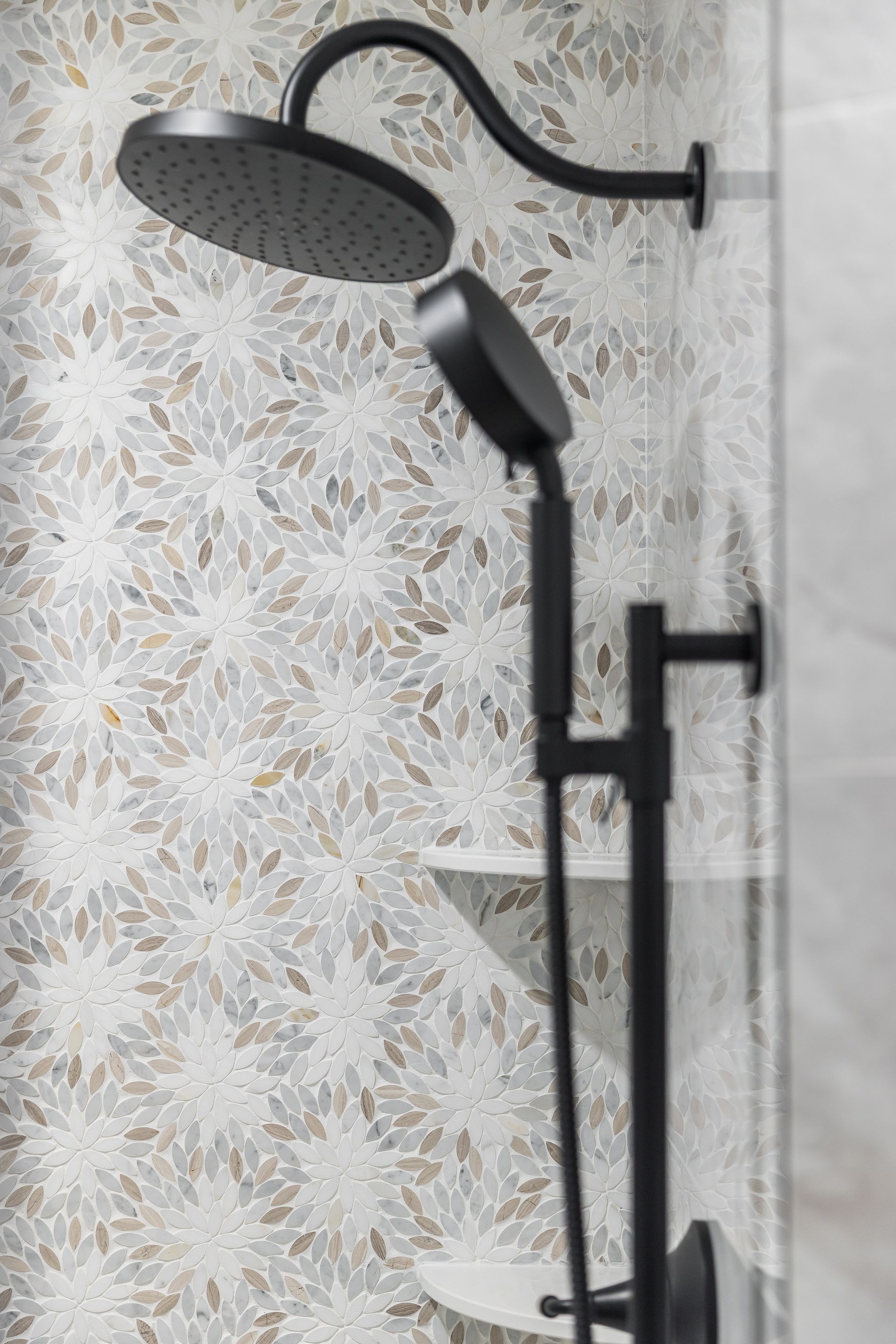 Black showerhead and handheld shower fixtures on patterned tile wall.