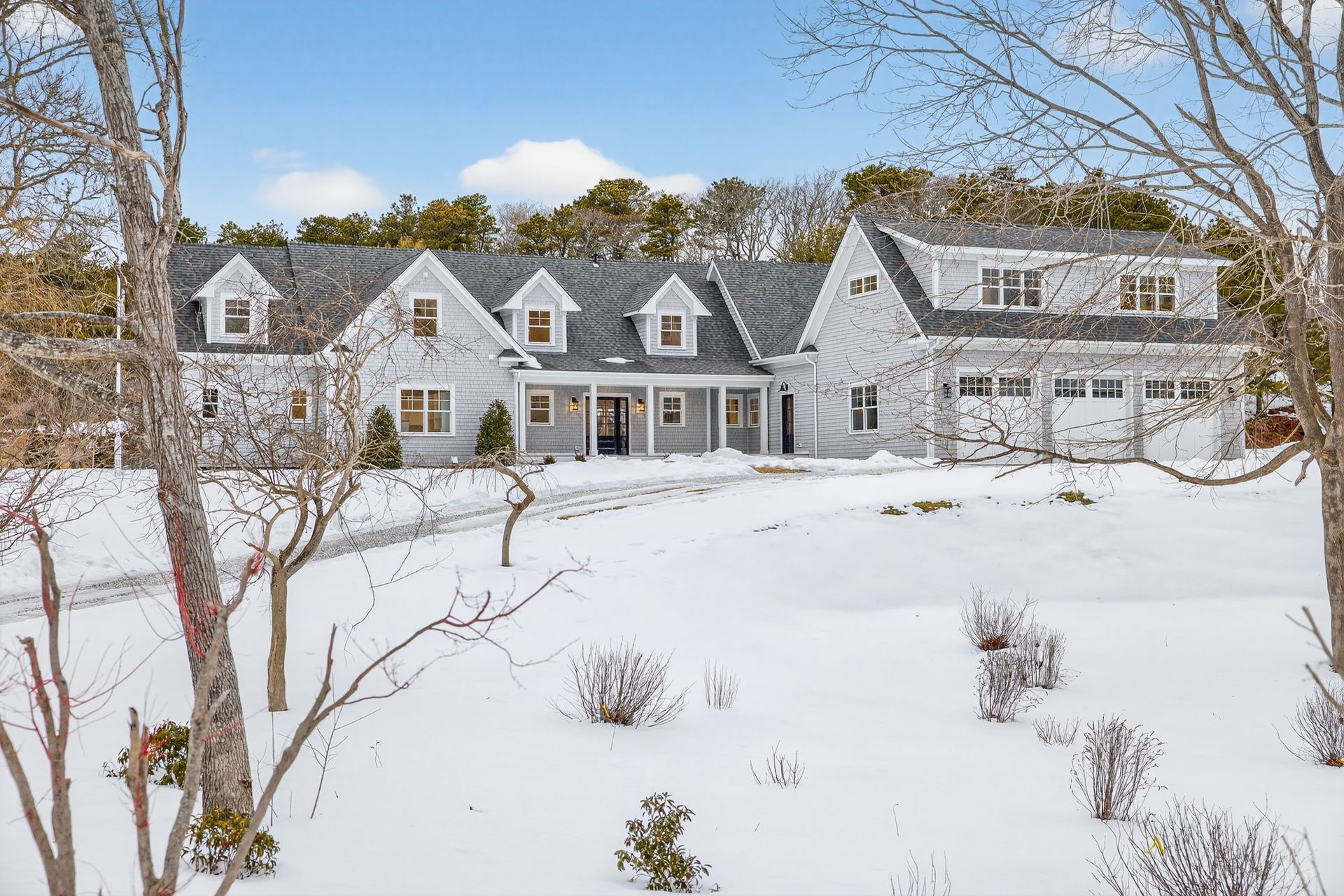 A light gray, multi-gable house with a white garage sits on a snow-covered lawn on a sunny day.