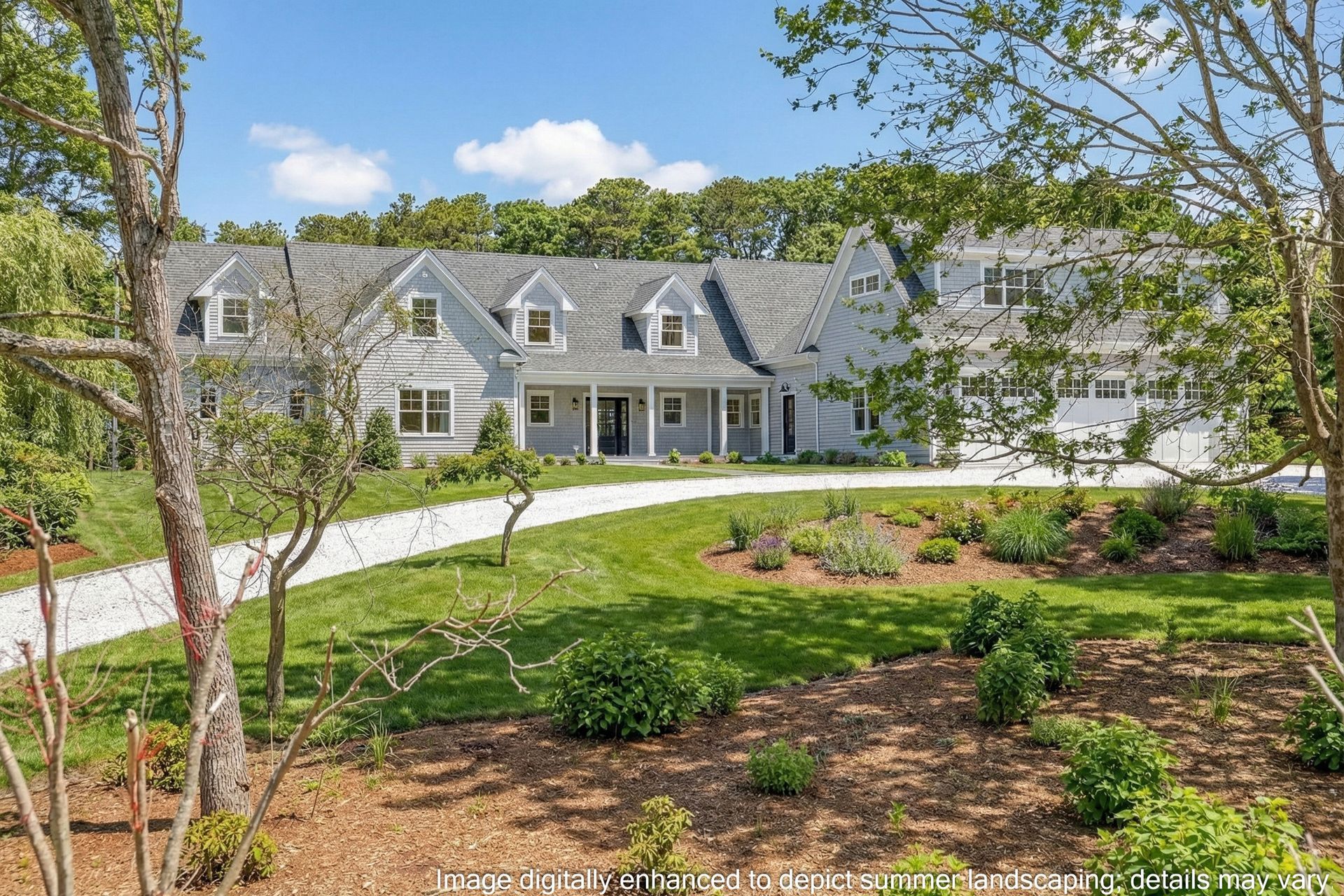 A light gray, multi-gable shingle-style house with a gravel driveway set amidst a lush green lawn and trees.
