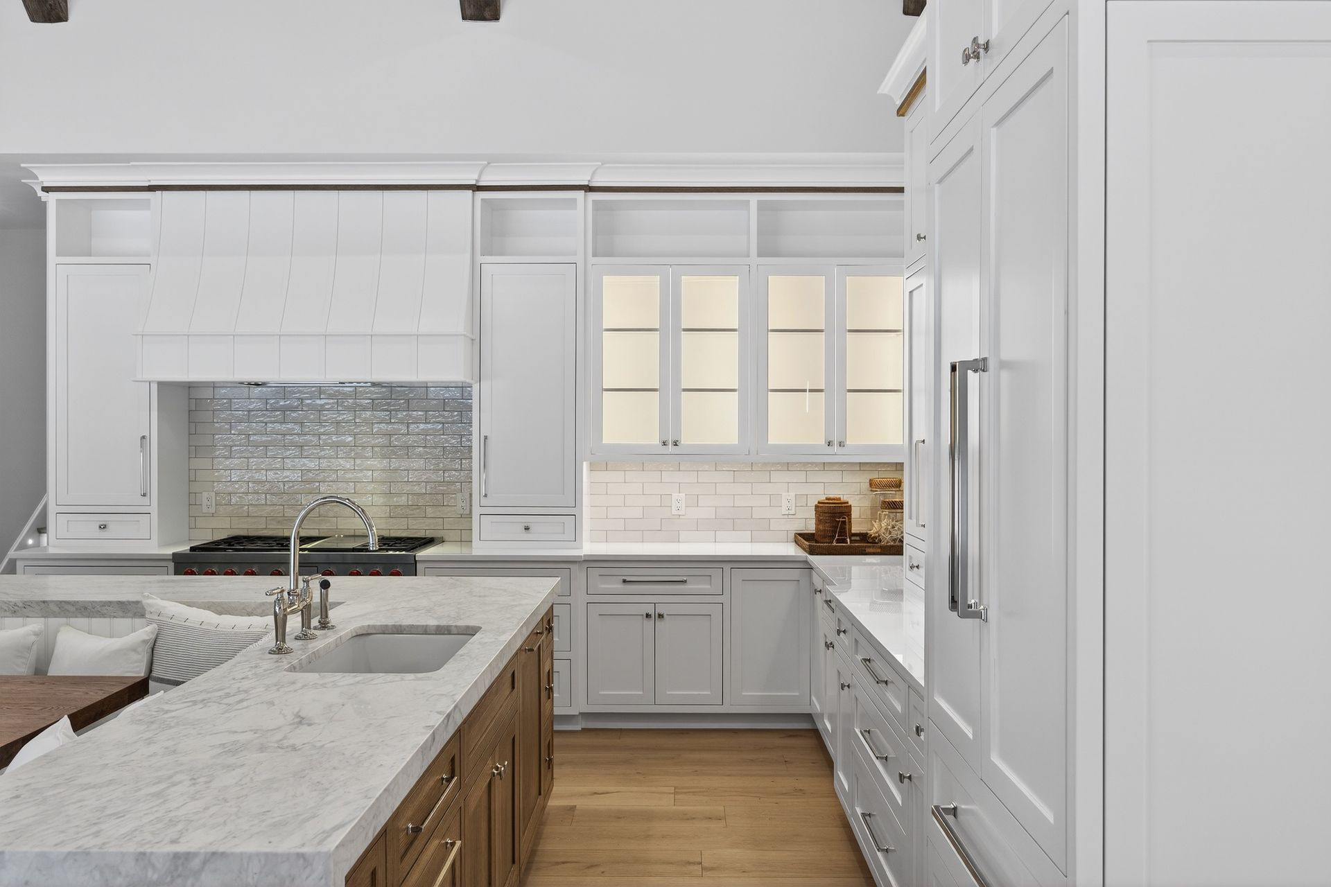 A bright kitchen featuring a white marble island, white shaker cabinets, wooden base cabinets, and a mosaic backsplash.