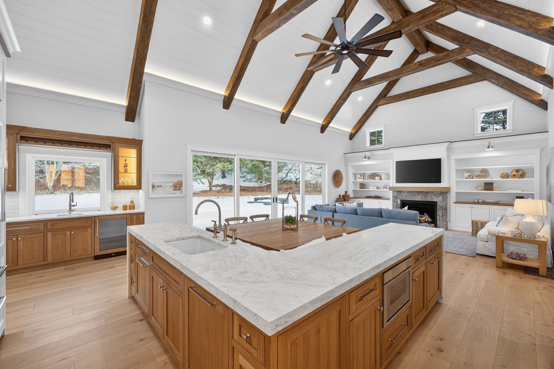 Open-concept kitchen and living area with wooden beams, large island, and glass doors to outside.
