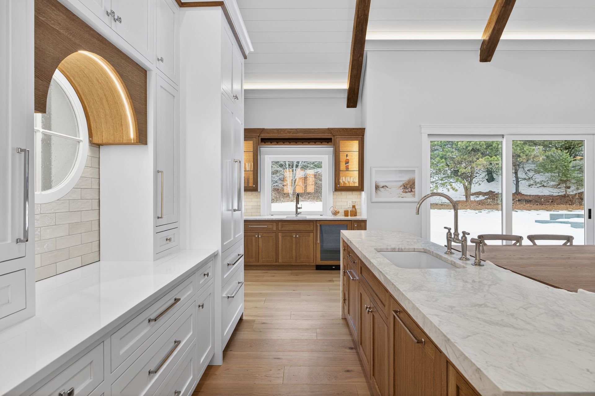 Kitchen with white cabinetry, wood accents, marble countertops, and a view to a backyard.
