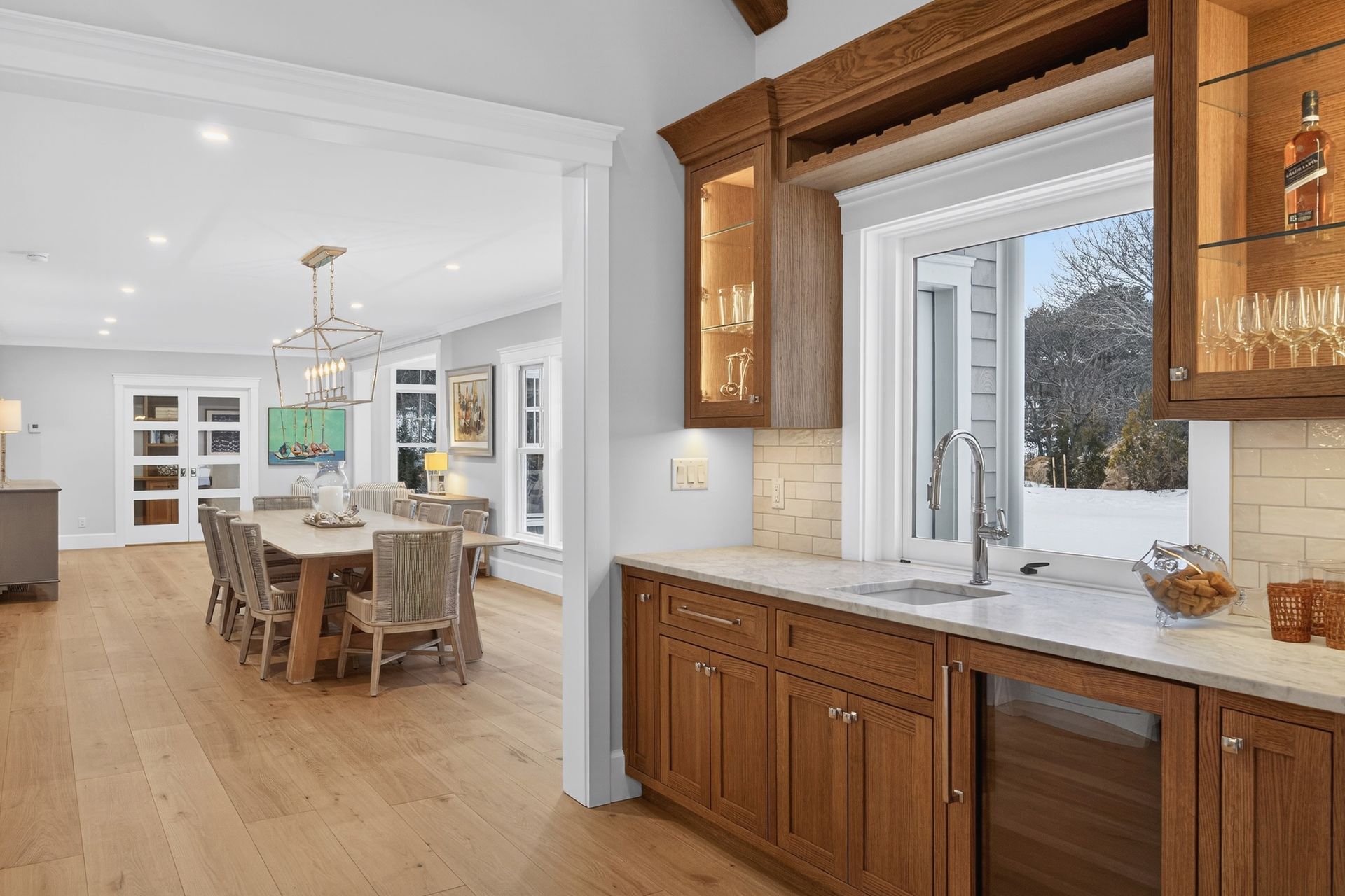 Wooden cabinets in a kitchen with a view into a dining area with a long table and chandelier.