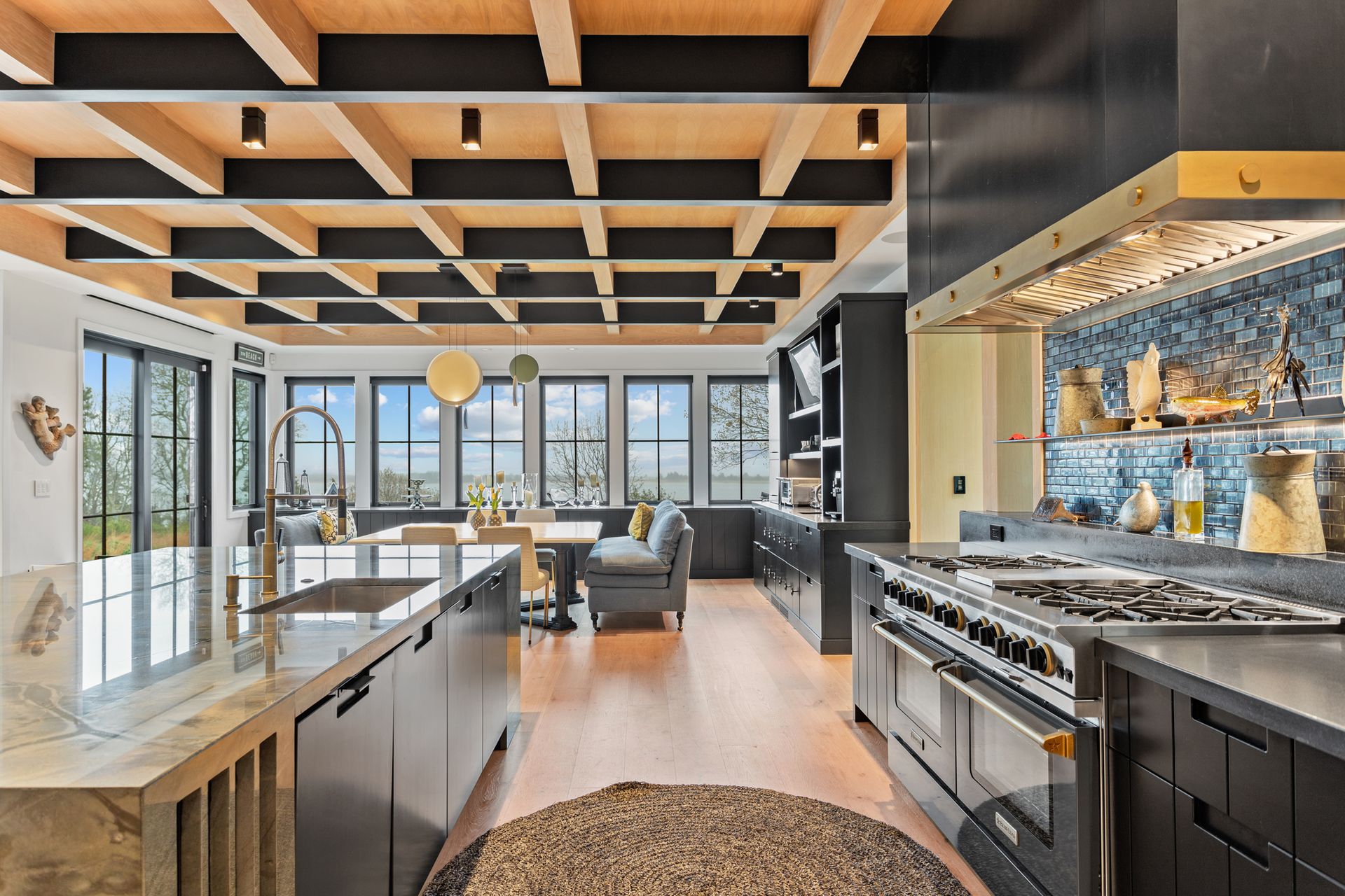 A modern, open-concept kitchen with a large island, stainless steel range, and a distinctive dark coffered wood ceiling.