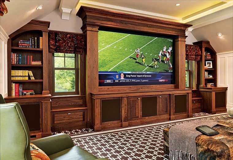 A large media room featuring a built-in wooden entertainment center with a TV displaying a football game and bookshelves.