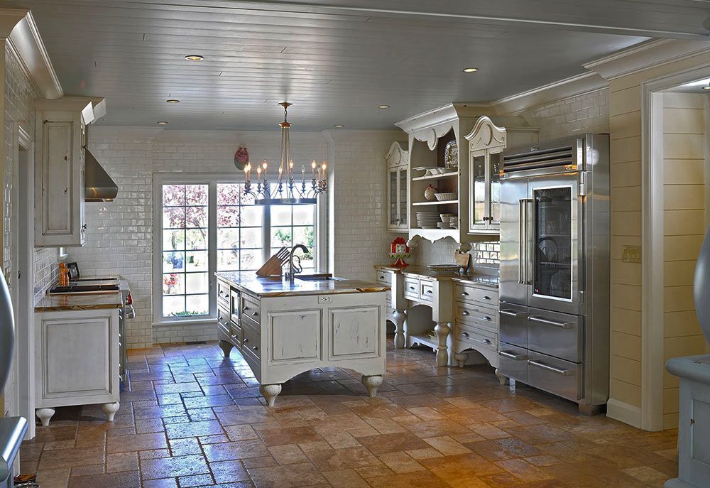 A rustic white kitchen with tile flooring, a central island, and stainless steel refrigerator.