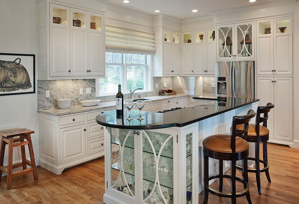 A kitchen with white cabinets, black countertops, wooden floors, a bar area with stools, and a window above the sink.