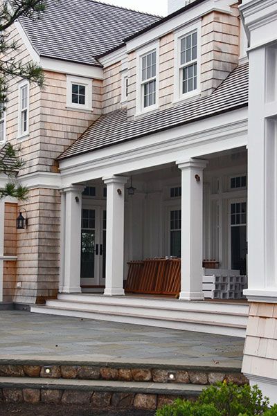 A two-story shingled home with a covered front porch featuring white columns and a stone patio with steps.