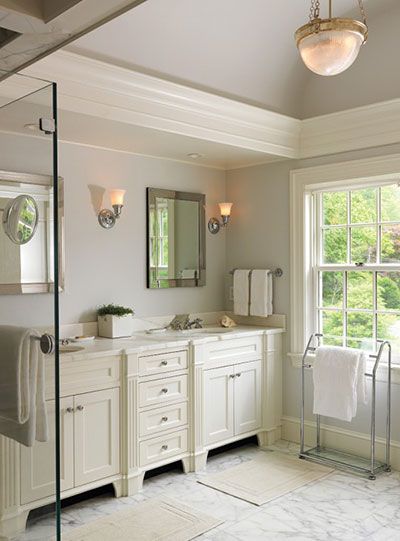 A bright, elegant bathroom with a white double vanity, marble floors, two mirrors with sconces, and a window with a towel rack.