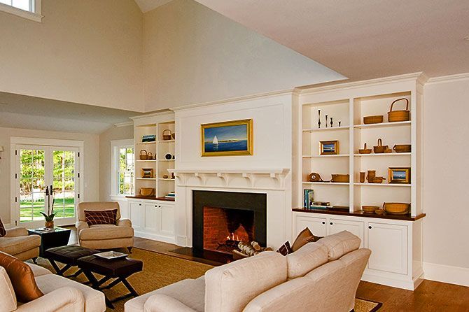 A bright living room with a fireplace, built-in white bookshelves, neutral furniture, and a painting of a sailboat.