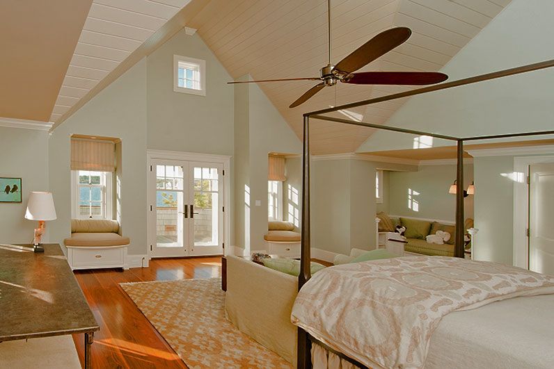 A spacious bedroom with a vaulted ceiling, a canopy bed, two window seats, and glass doors leading to an outdoor deck.