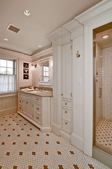 A bright, classic-style bathroom featuring a white vanity, cabinetry, tiled flooring with accent patterns, and a shower.
