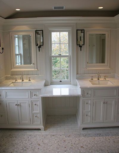 A double bathroom vanity with white cabinets, marble countertops, and mirrors flanking a central window.