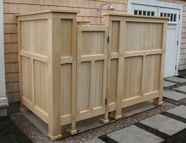 An outdoor shower enclosure with light wood paneling, featuring a gated entrance, set against a house exterior.