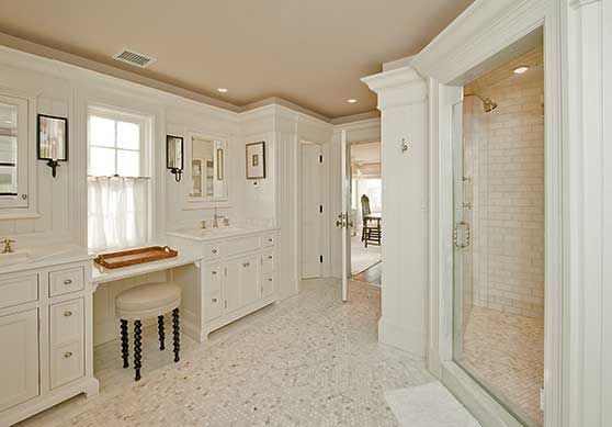 A bright white bathroom featuring a marble floor, double vanity with a makeup desk, and a glass-enclosed shower.