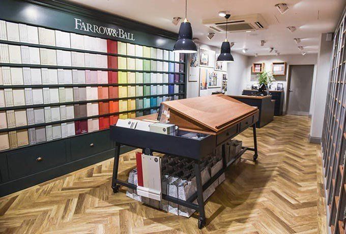 A Farrow & Ball paint showroom features a large wall display of color swatches and a central wooden-topped service desk.