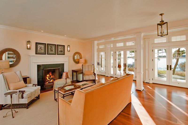 A bright living room with a fireplace, orange sofa, cream-colored armchair, and large glass doors opening to the outdoors.