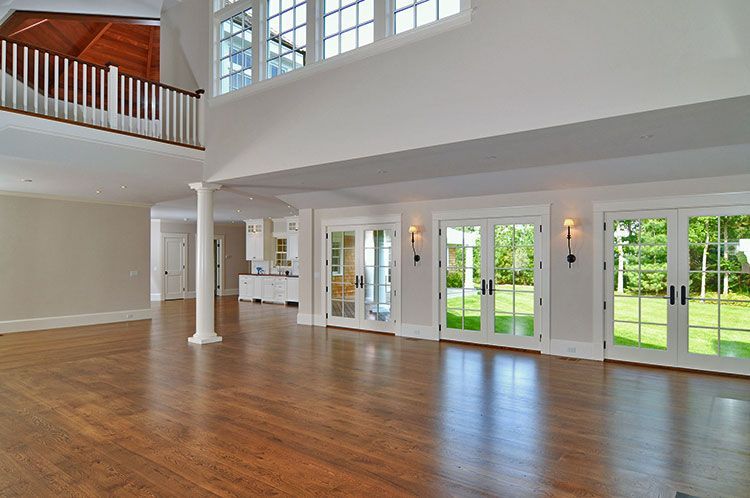 A spacious, well-lit room with hardwood floors, a white pillar, and double glass doors leading to a green backyard.