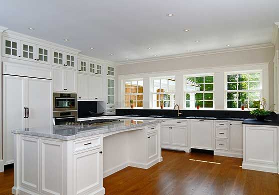 A bright, spacious kitchen featuring white cabinetry, a large marble-topped island, dark countertops, and wood flooring.