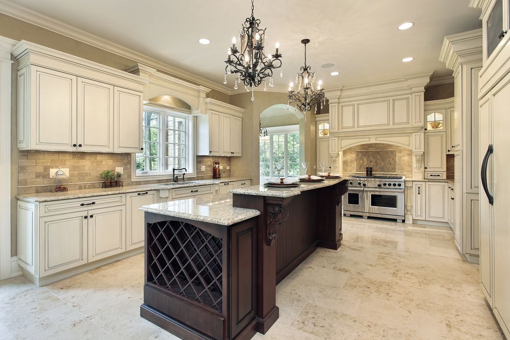 Elegant kitchen with cream-colored cabinetry, a dark wood central island with built-in wine storage, and chandeliers.