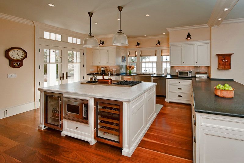 Bright, spacious kitchen with a large white island containing a microwave and wine cooler, dark countertops, and wood floor.