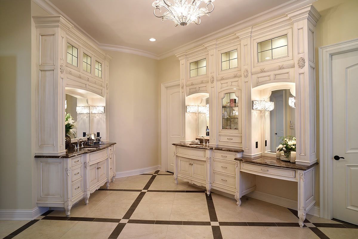 A luxurious bathroom with off-white ornate cabinetry, marble countertops, dual vanities, and tiled floors.