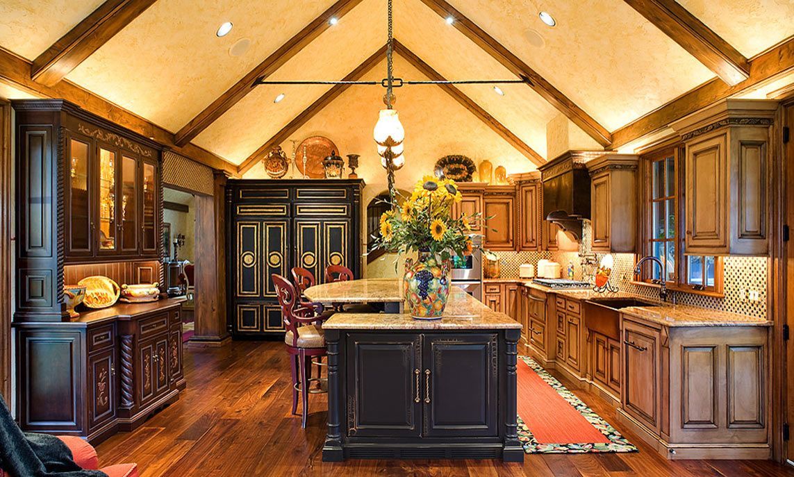 A rustic, spacious kitchen with dark wooden cabinets, a central island, vaulted ceiling beams, and warm ambient lighting.