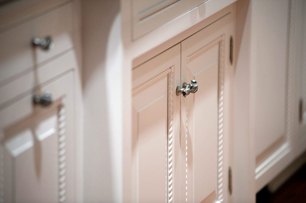 Close-up of cream-colored kitchen cabinets with silver knobs and decorative fluted detailing.