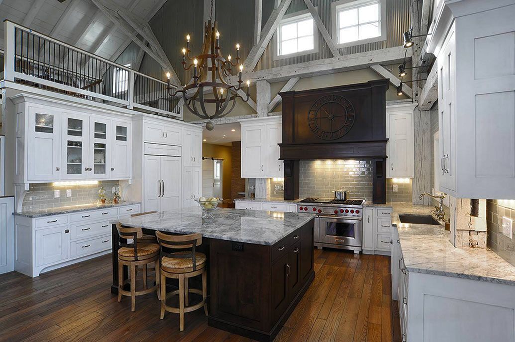 A farmhouse kitchen with a large dark wood island, white cabinets, a prominent range hood, and a rustic chandelier.