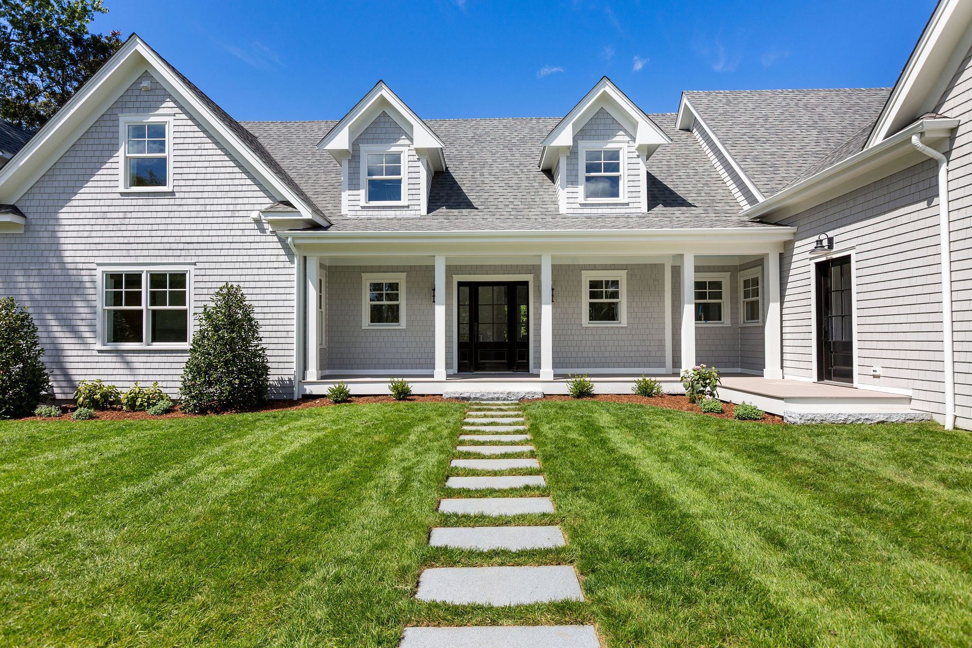 A light gray farmhouse with a stone walkway leading to the front door, surrounded by a vibrant green lawn.