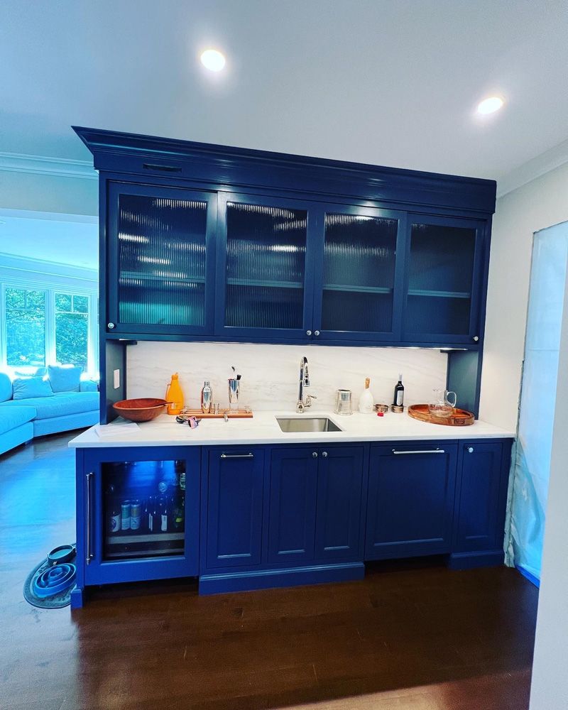 A blue wet bar featuring glass-front cabinets, a white countertop, a small sink, and a built-in beverage refrigerator.