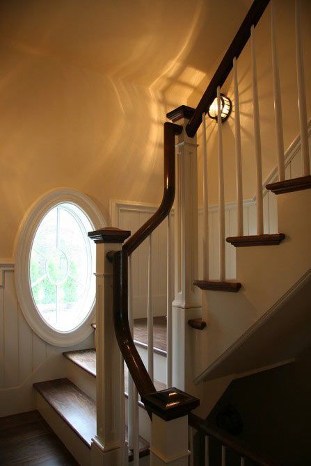 An interior view of a wooden staircase with a white railing and an oval window on the left side.