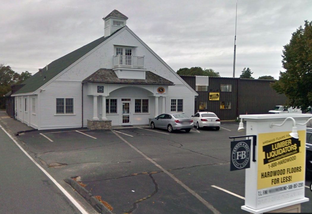 A white colonial-style building with a parking lot and a sign for Lumber Liquidators in the foreground.