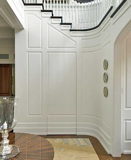 A white curved staircase wall with wood paneling and decorative plates in a classic interior entryway.