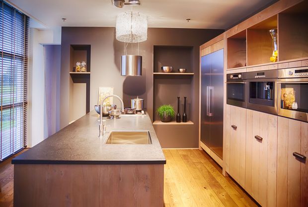 A modern kitchen with a wooden island, grey countertop, integrated appliances, and warm lighting in a minimalist design.