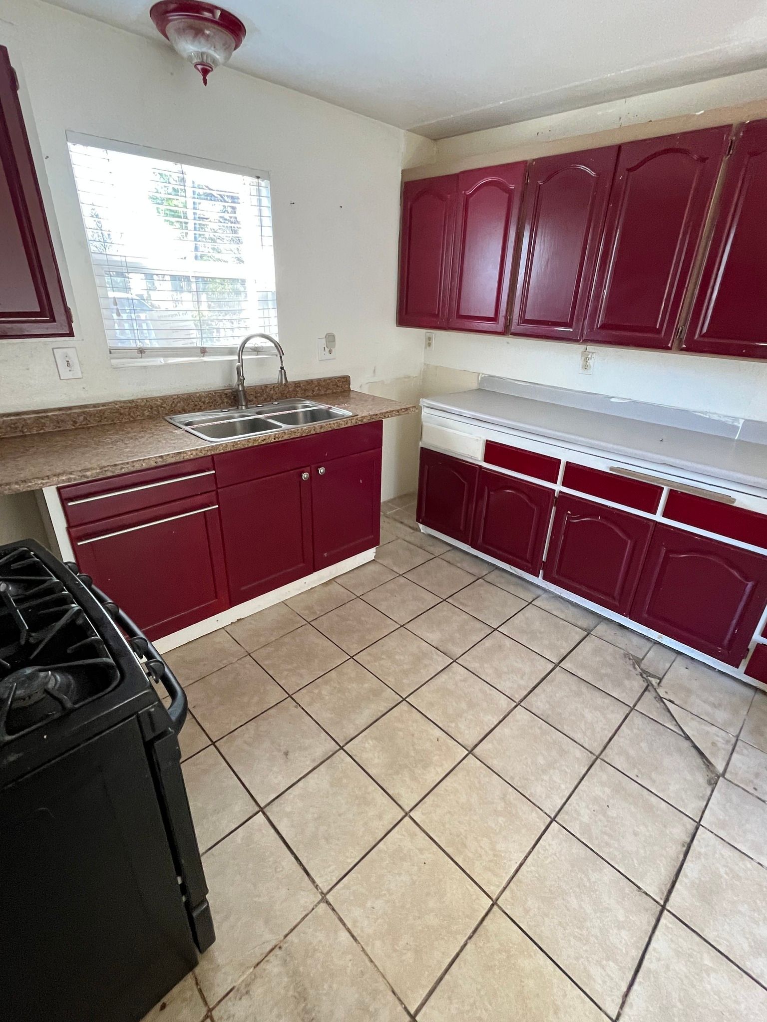 Small kitchen with burgundy cabinets, tiled floor, black stove, and window over the sink.