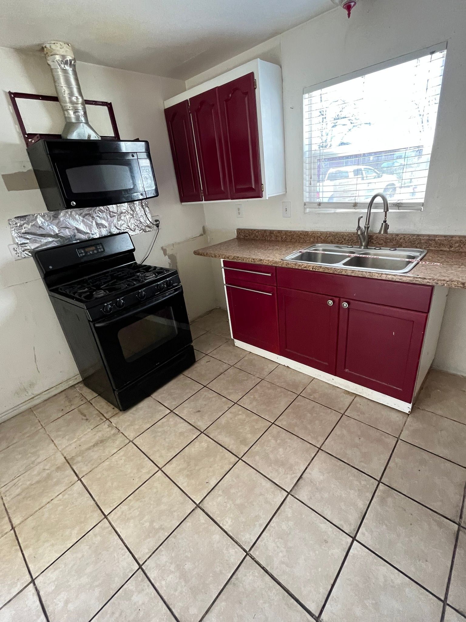 Small kitchen with black stove, red cabinets, beige tile floor, and a window over the sink.