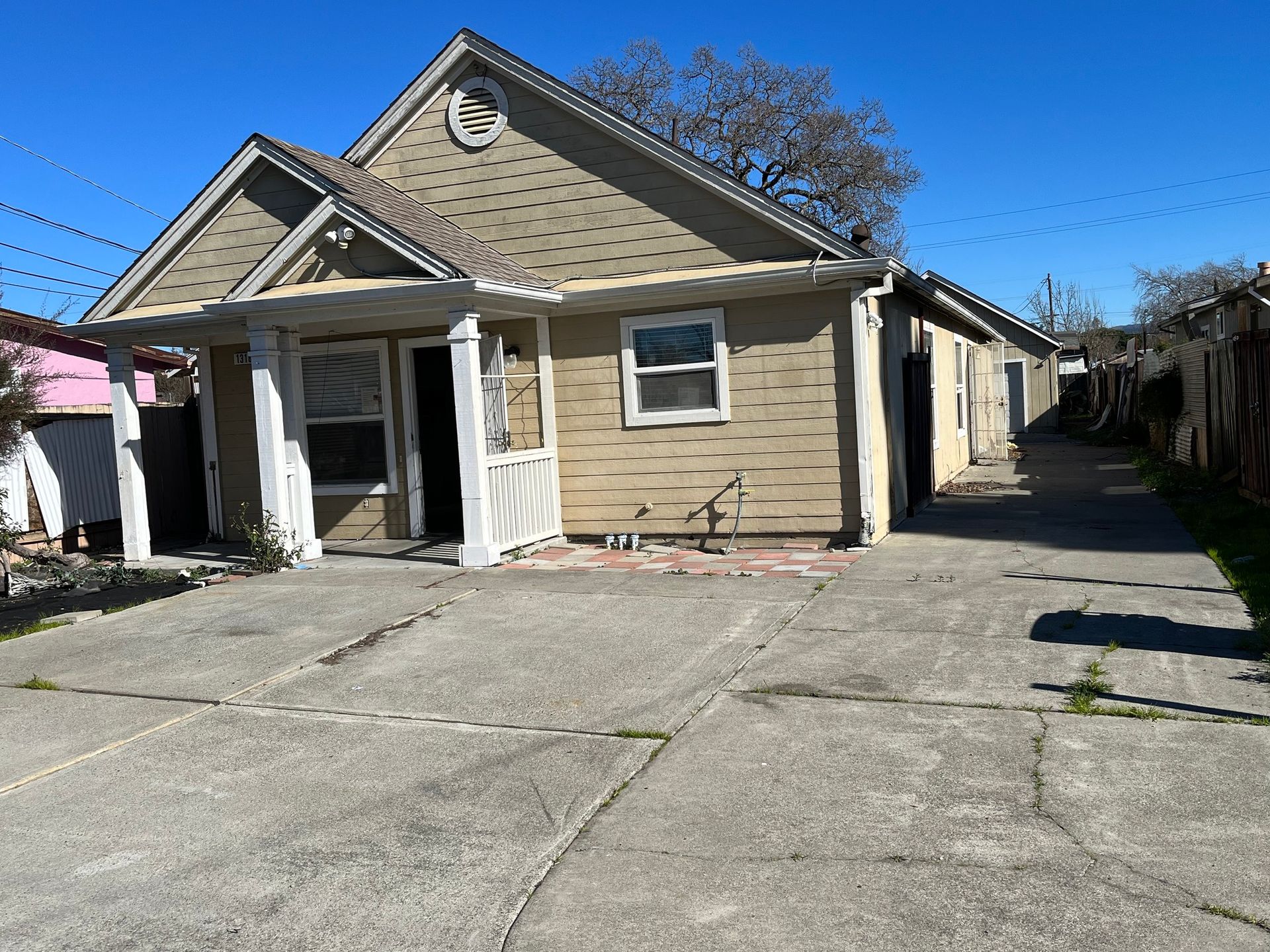 Beige house with front porch and driveway under a clear blue sky